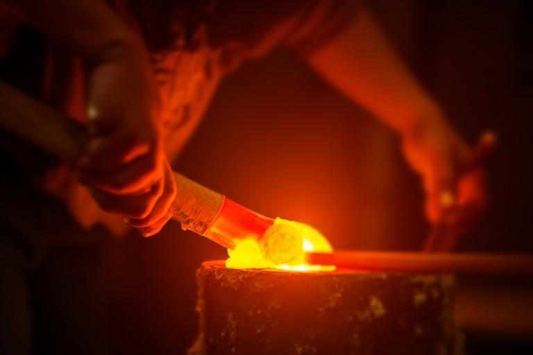 Molten glass being heated in a vibrant furnace at a glass art studio. Skilled artisan carefully working with the heat.